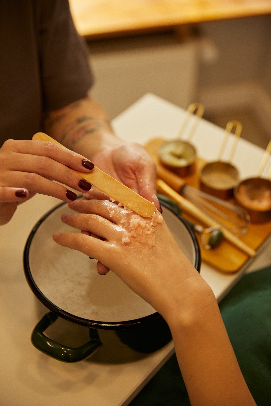 Zabieg dloni przy cieplej misie z mosieznymi lyzeczkami i ciemnym manicure